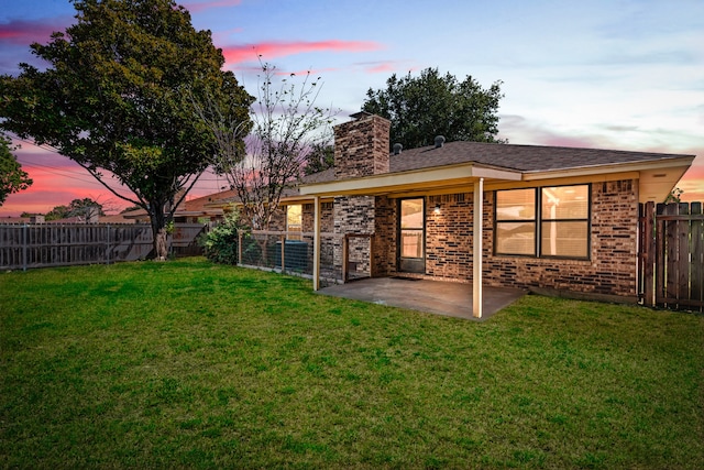 back house at dusk featuring a patio and a lawn