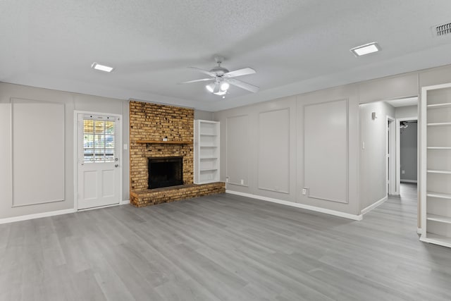 unfurnished living room with a textured ceiling, a brick fireplace, ceiling fan, and light hardwood / wood-style flooring