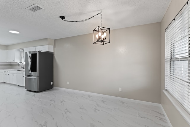 kitchen with stainless steel refrigerator, a chandelier, decorative light fixtures, sink, and white cabinetry