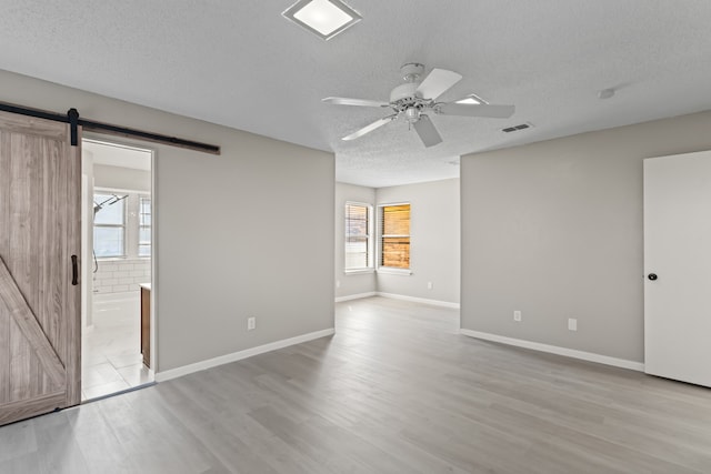 unfurnished room featuring ceiling fan, a textured ceiling, light wood-type flooring, and a barn door