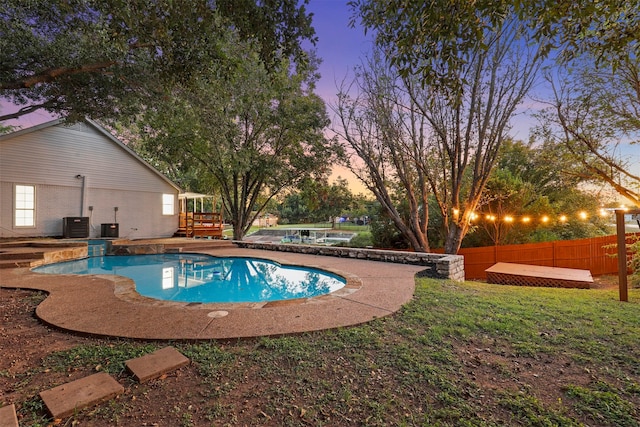 pool at dusk with cooling unit, a deck, and a yard