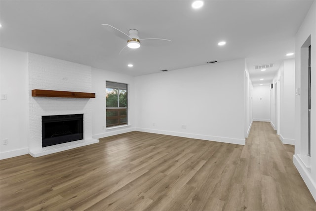 unfurnished living room with ceiling fan, light wood-type flooring, and a brick fireplace