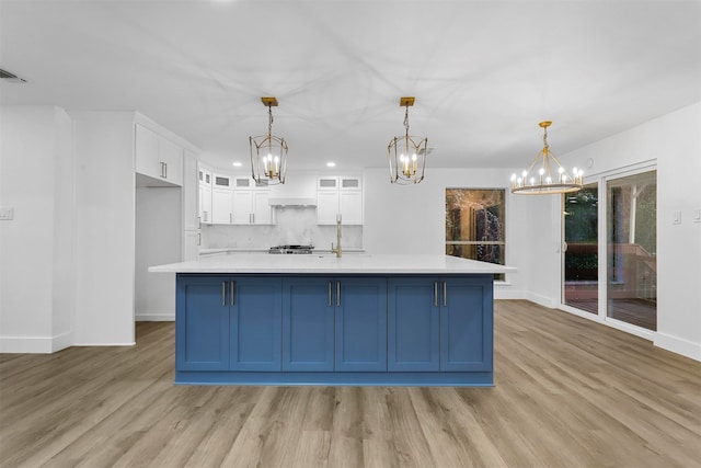 kitchen featuring white cabinets, a large island with sink, hanging light fixtures, and light hardwood / wood-style floors