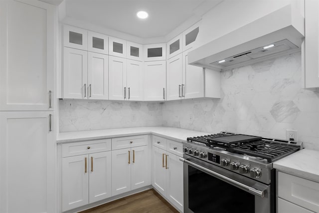 kitchen featuring light stone counters, custom exhaust hood, white cabinetry, and high end range