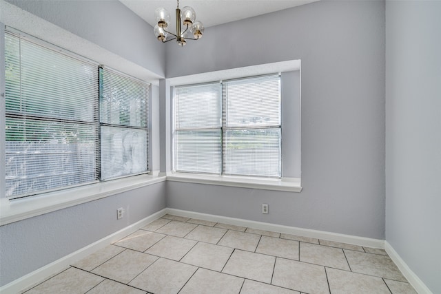 tiled spare room featuring an inviting chandelier