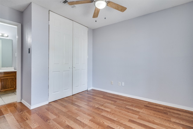 unfurnished bedroom featuring light hardwood / wood-style floors, ceiling fan, ensuite bathroom, and a closet