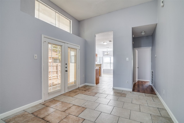 foyer entrance featuring french doors, an inviting chandelier, light tile patterned floors, and a wealth of natural light