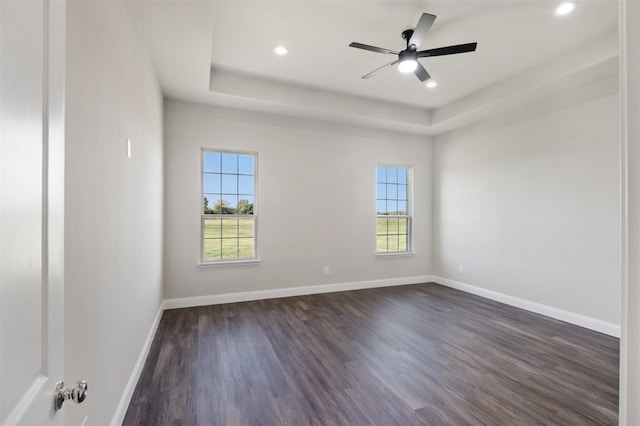 unfurnished room with a raised ceiling, ceiling fan, and dark wood-type flooring