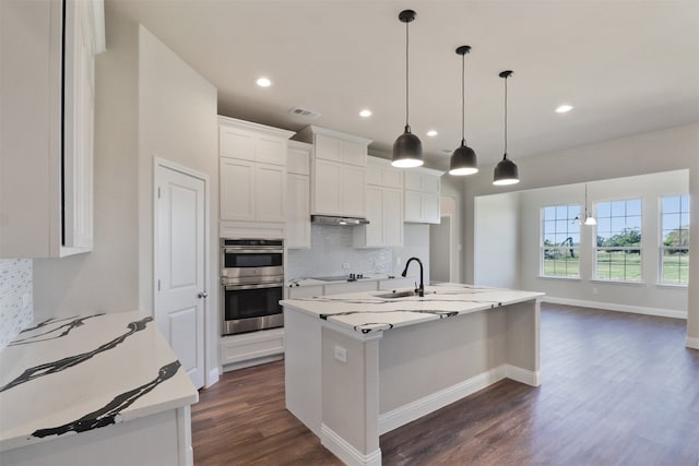 kitchen with a kitchen island with sink, double oven, decorative light fixtures, decorative backsplash, and white cabinets