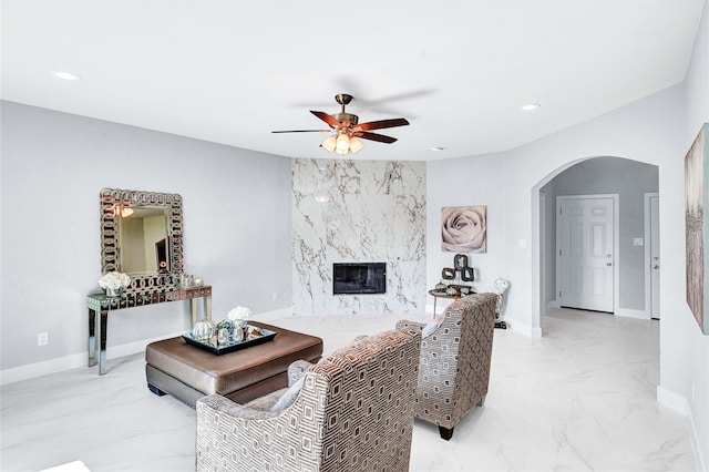 living room with a high end fireplace and ceiling fan