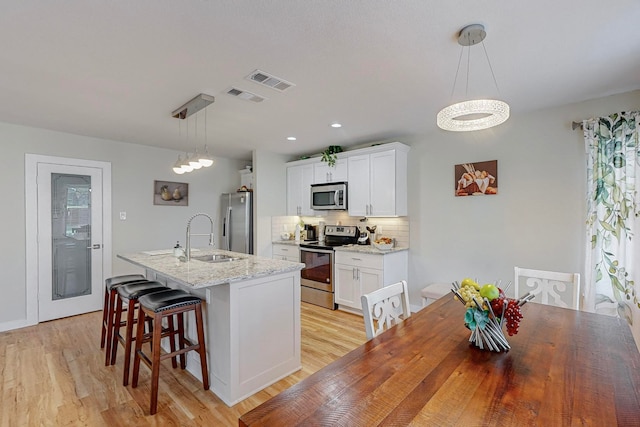 kitchen with appliances with stainless steel finishes, hanging light fixtures, white cabinets, sink, and a notable chandelier