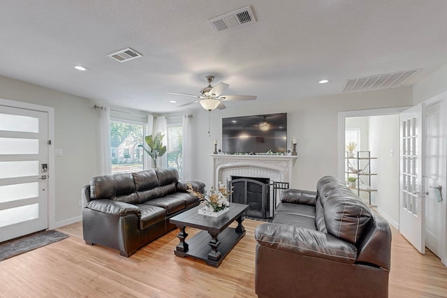 living room featuring a textured ceiling, ceiling fan, light hardwood / wood-style flooring, and a brick fireplace