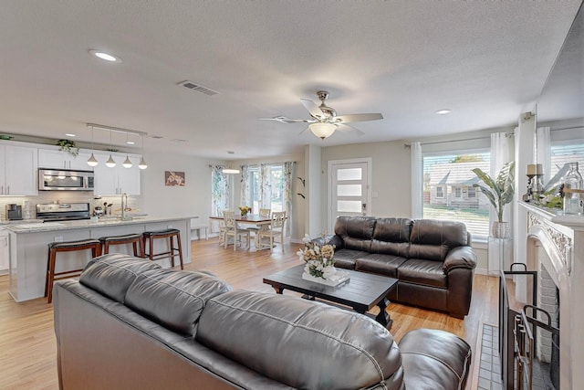 living room with a wealth of natural light, light hardwood / wood-style floors, ceiling fan, and a textured ceiling