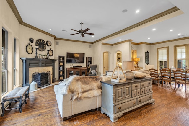 living room with ceiling fan, crown molding, dark hardwood / wood-style flooring, and a tile fireplace