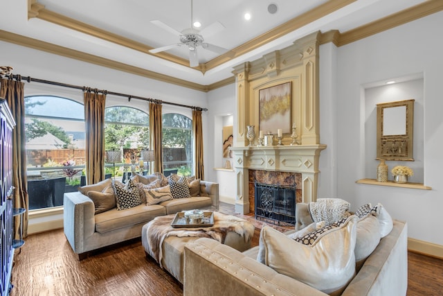 living room with ceiling fan, ornamental molding, a premium fireplace, dark wood-type flooring, and a tray ceiling