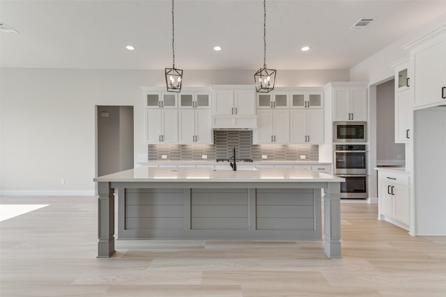 kitchen featuring white cabinets, stainless steel appliances, light hardwood / wood-style flooring, decorative light fixtures, and a spacious island