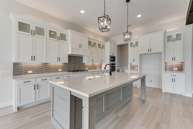 kitchen featuring hanging light fixtures, decorative backsplash, a kitchen island with sink, and white cabinets