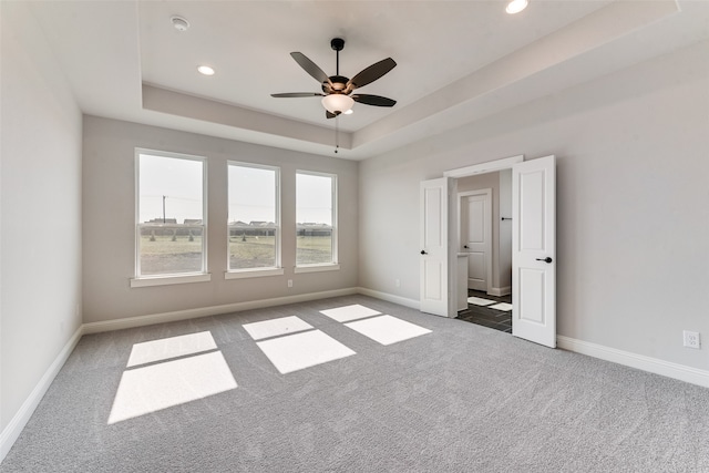 carpeted spare room with ceiling fan and a raised ceiling