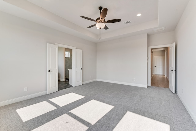 unfurnished bedroom featuring a tray ceiling, dark colored carpet, and ceiling fan