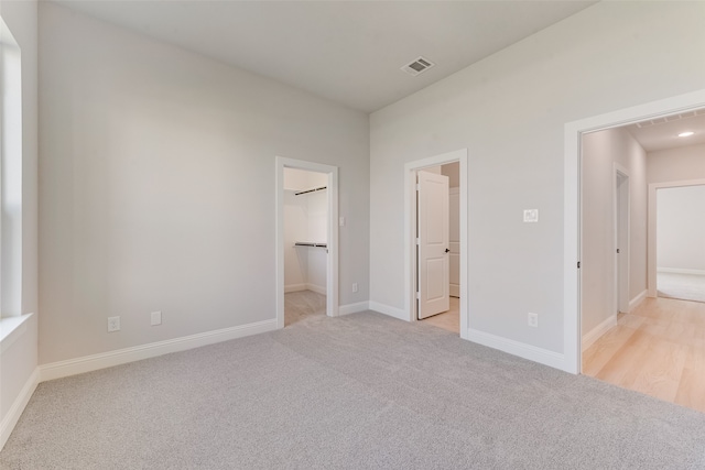 unfurnished bedroom with a spacious closet, connected bathroom, a closet, and light carpet