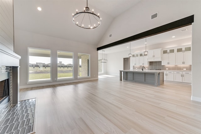 unfurnished living room with an inviting chandelier, light hardwood / wood-style flooring, sink, and high vaulted ceiling