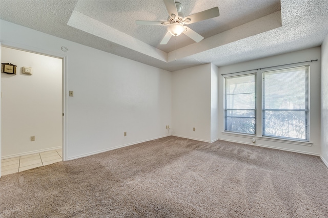 empty room featuring light colored carpet, ceiling fan, a raised ceiling, and a textured ceiling