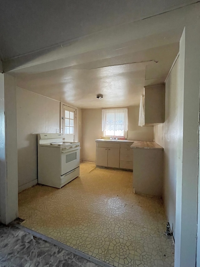 kitchen featuring sink, white range, light tile patterned floors, and white cabinetry