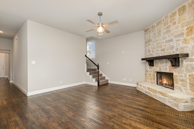 unfurnished living room featuring a stone fireplace, dark hardwood / wood-style floors, and ceiling fan