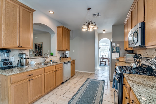 kitchen with light stone counters, sink, backsplash, appliances with stainless steel finishes, and an inviting chandelier