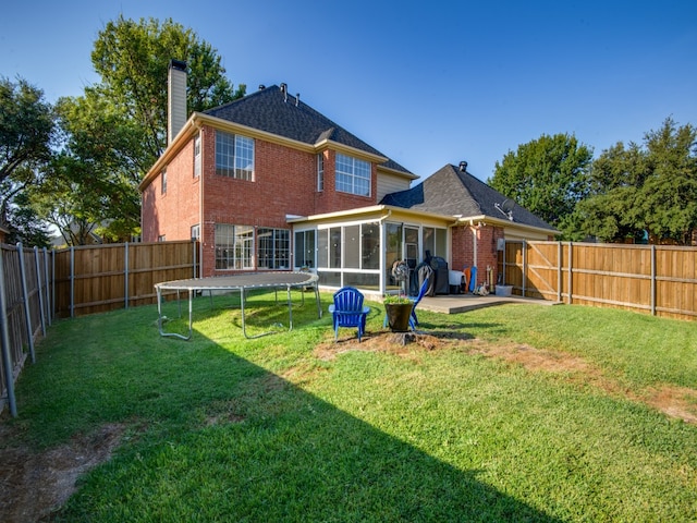 rear view of property with a sunroom, a patio, a trampoline, and a lawn