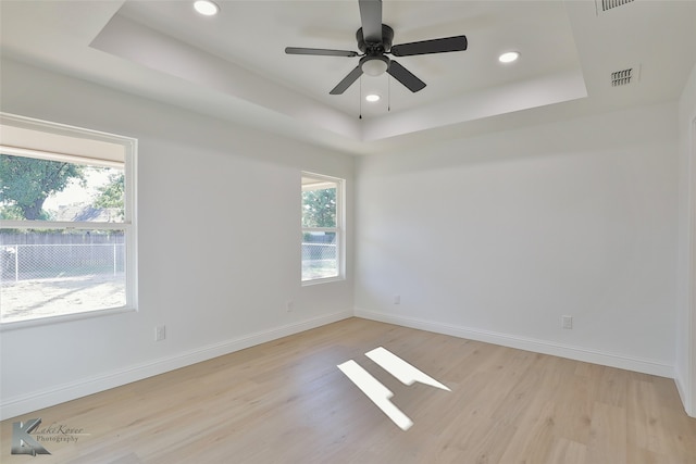 empty room featuring light hardwood / wood-style flooring, ceiling fan, a tray ceiling, and a wealth of natural light