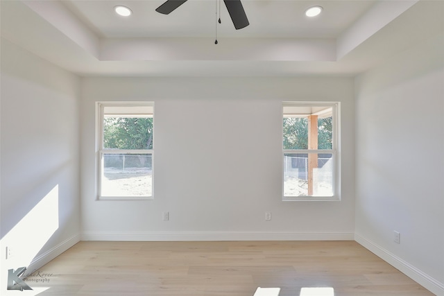 unfurnished room featuring light hardwood / wood-style floors, a healthy amount of sunlight, a tray ceiling, and ceiling fan