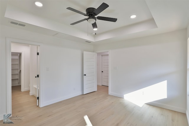 unfurnished bedroom featuring a spacious closet, a closet, light wood-type flooring, and ceiling fan