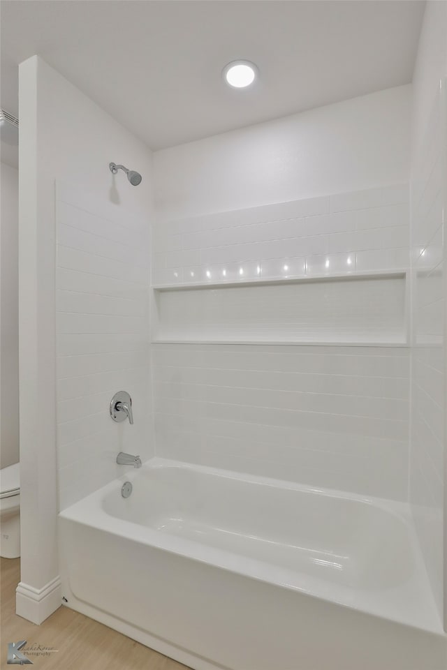 bathroom with toilet, hardwood / wood-style flooring, and tiled shower / bath