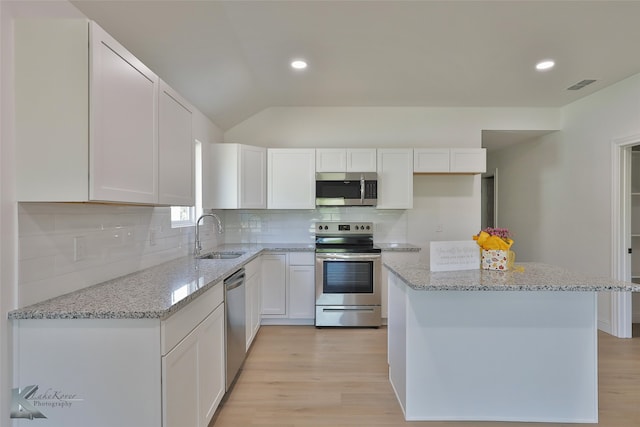 kitchen with appliances with stainless steel finishes, white cabinetry, light stone countertops, light hardwood / wood-style floors, and sink