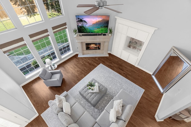 living room with a premium fireplace, dark hardwood / wood-style flooring, a towering ceiling, and ceiling fan