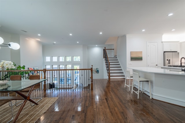 kitchen with ornamental molding, dark wood-type flooring, white cabinetry, stainless steel refrigerator with ice dispenser, and a breakfast bar area