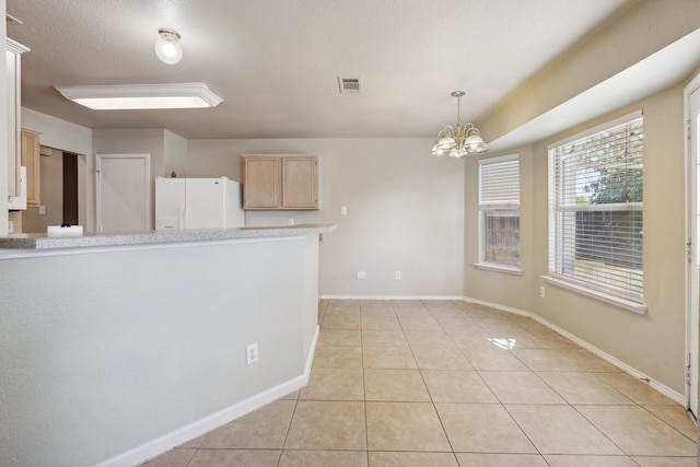 kitchen featuring light tile patterned flooring, a textured ceiling, a chandelier, light brown cabinetry, and white fridge