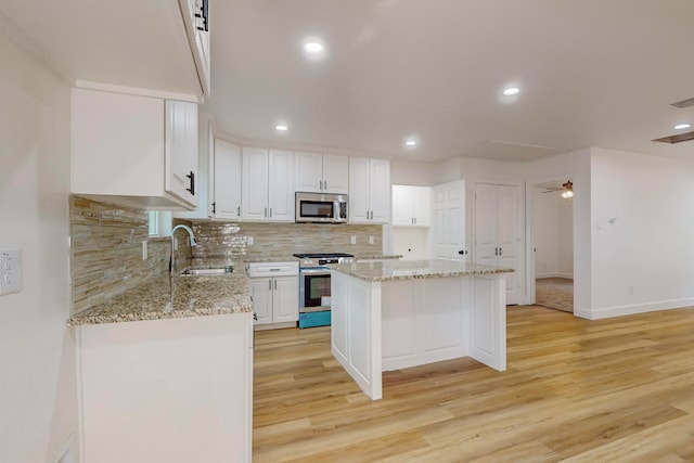 kitchen with a kitchen island, stainless steel appliances, white cabinets, sink, and light hardwood / wood-style flooring