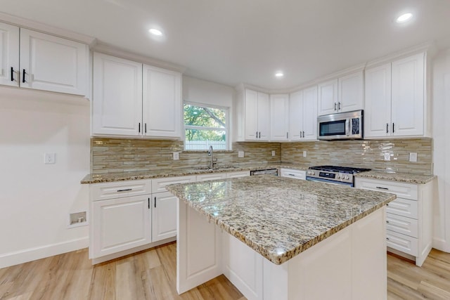 kitchen with a kitchen island, white cabinetry, stainless steel appliances, and light wood-type flooring