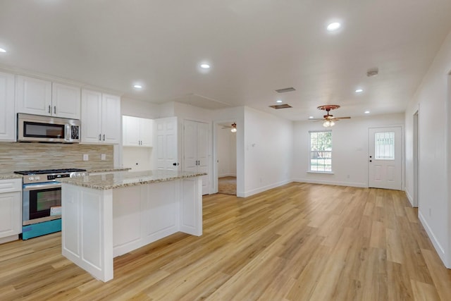 kitchen featuring light wood-type flooring, ceiling fan, a center island, white cabinets, and appliances with stainless steel finishes