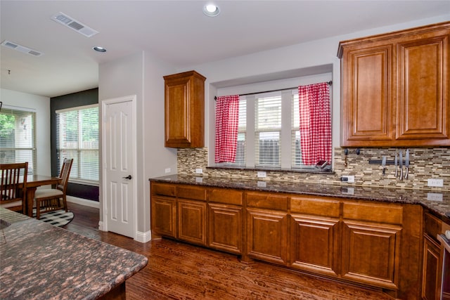 kitchen featuring dark stone counters, dark hardwood / wood-style flooring, decorative backsplash, and a wealth of natural light