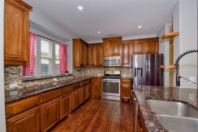 kitchen with stainless steel appliances, dark stone countertops, dark wood-type flooring, and tasteful backsplash