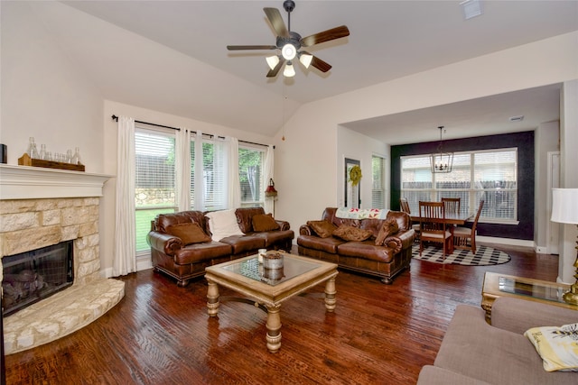 living room with ceiling fan with notable chandelier, lofted ceiling, a stone fireplace, and dark hardwood / wood-style flooring