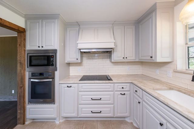 kitchen with light stone countertops, decorative backsplash, stainless steel appliances, white cabinets, and custom exhaust hood