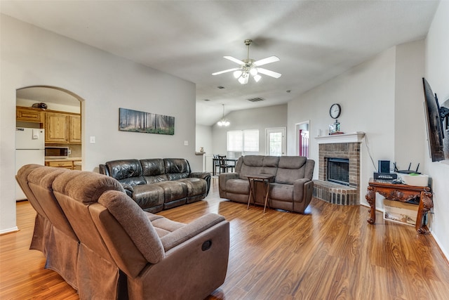 living room featuring ceiling fan, light hardwood / wood-style flooring, a fireplace, and vaulted ceiling