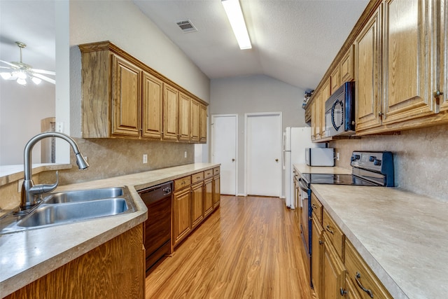 kitchen with light wood-type flooring, black appliances, sink, vaulted ceiling, and a textured ceiling