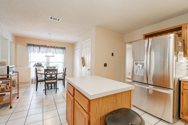 kitchen with pendant lighting, a kitchen island, stainless steel appliances, light tile patterned floors, and a textured ceiling