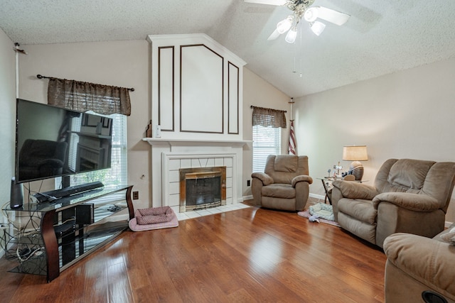 living room with ceiling fan, a tile fireplace, hardwood / wood-style floors, vaulted ceiling, and a textured ceiling