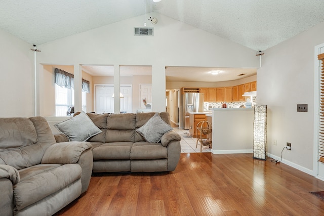 living room with a textured ceiling, light hardwood / wood-style flooring, and high vaulted ceiling